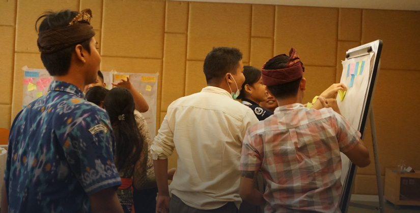 Several youth in Indonesia gather around a flip chart with post-it notes