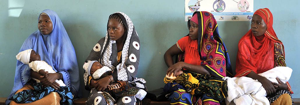 Four women waiting with their infants at a health facility.